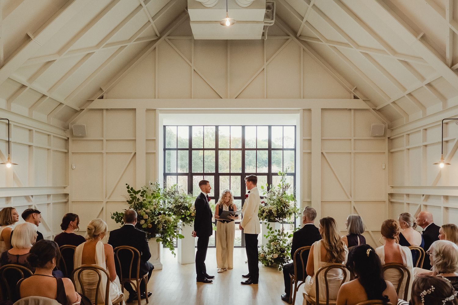 A bright white chapel interior with vaulted ceilings and wooden beams hosts an intimate wedding ceremony.