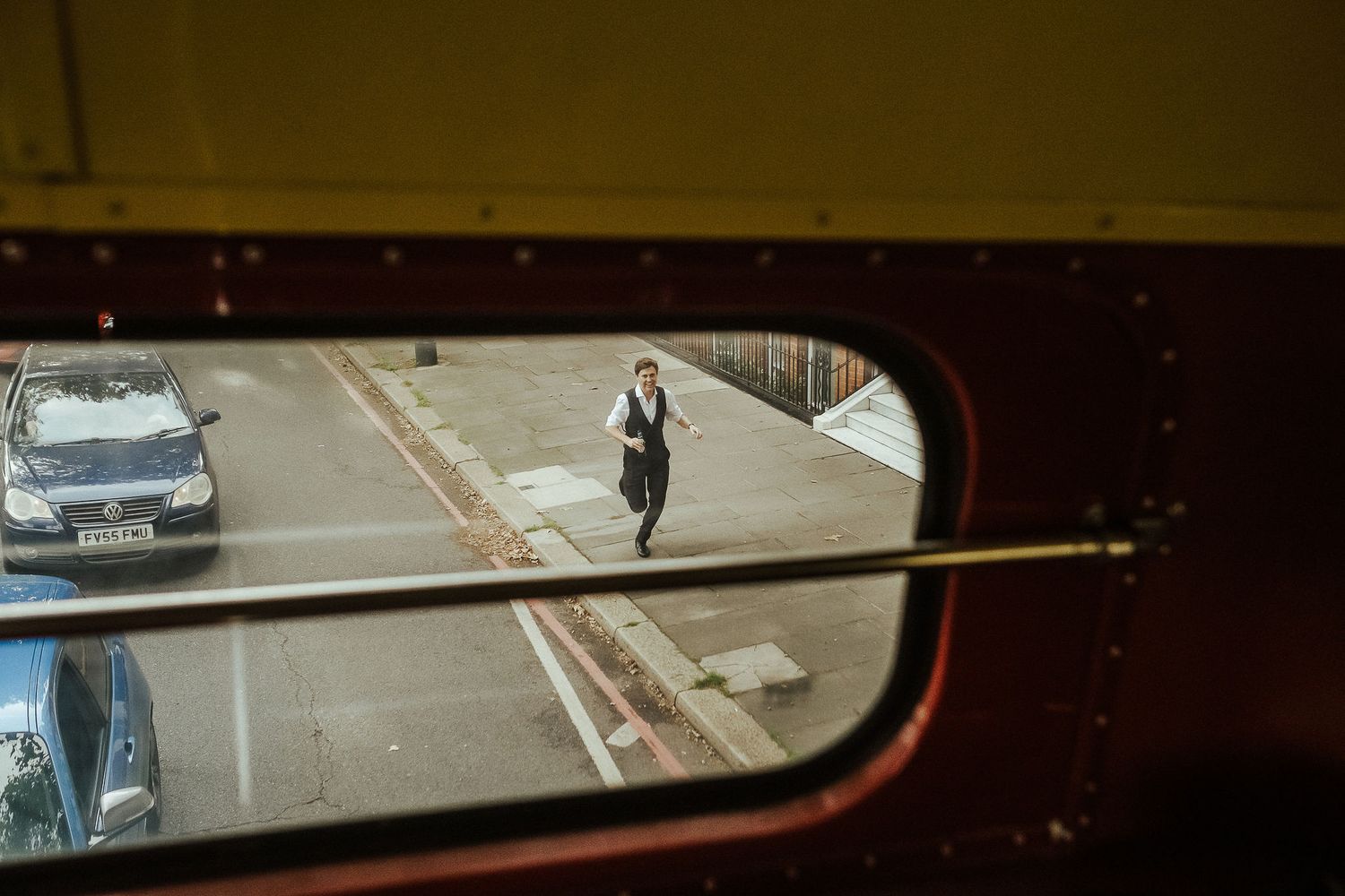View through a rearview mirror showing a person walking on a city street with buildings in the background.