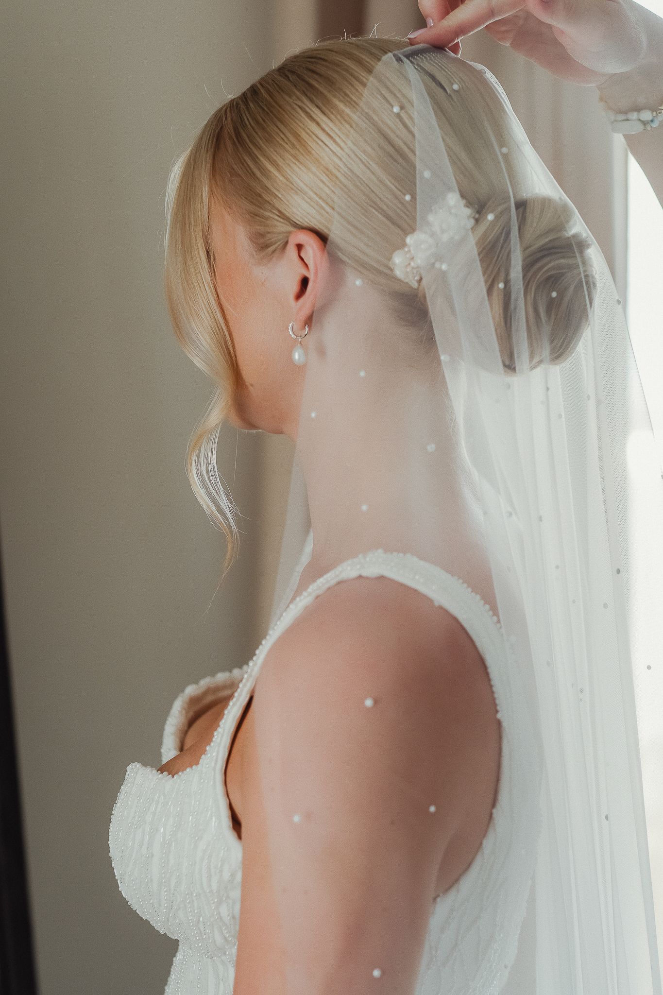 A bride in a white wedding dress gets help adjusting her delicate veil in a series of elegant preparation shots.
