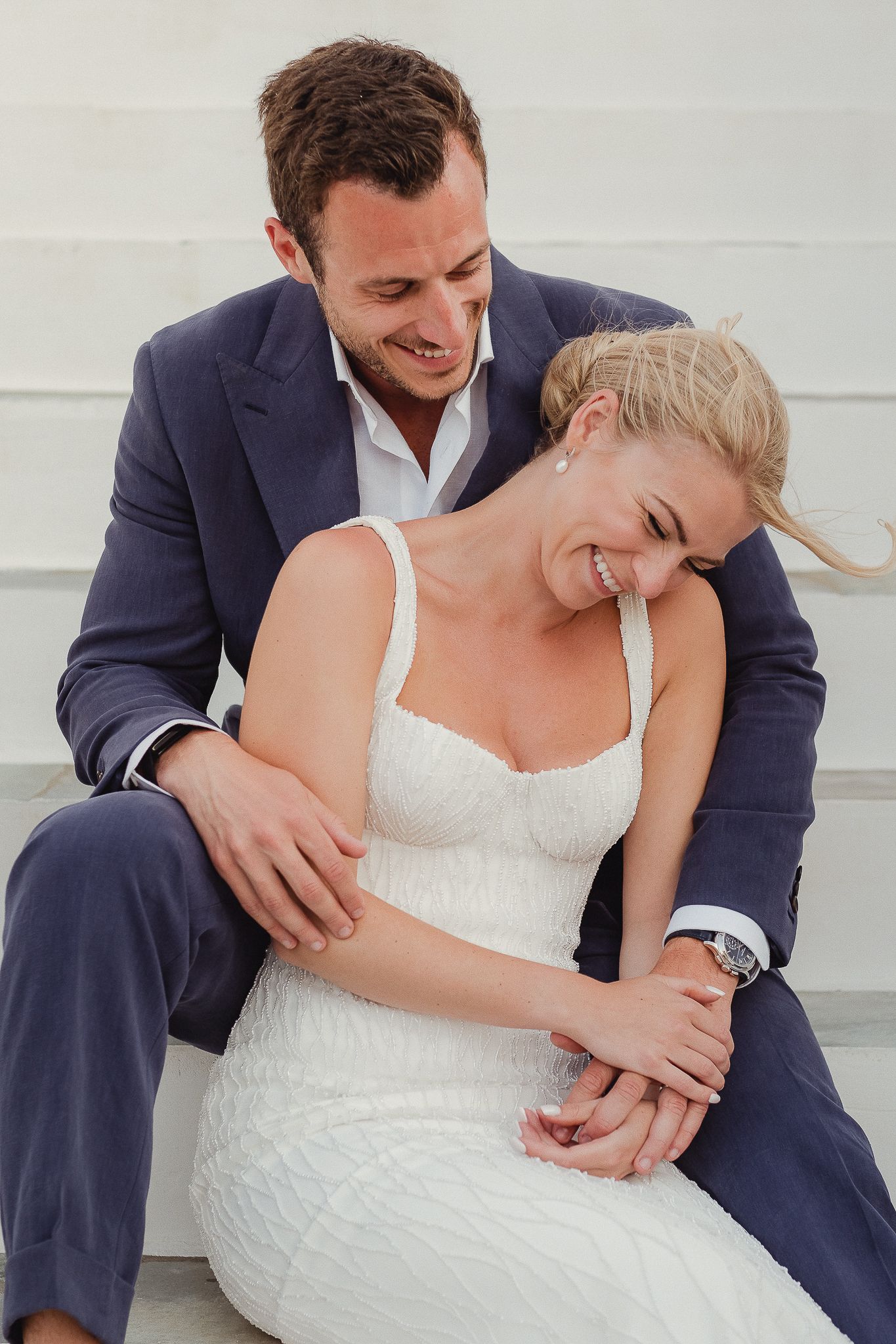 A couple in formal wedding attire share intimate candid moments while seated on white steps.