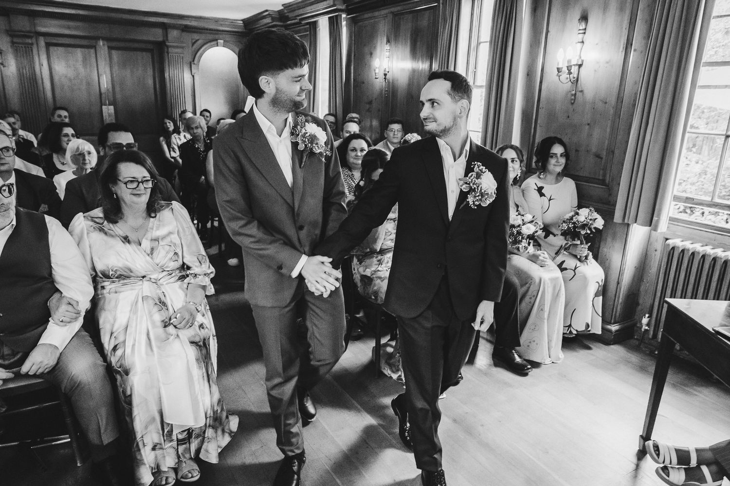 Black and white photo of a joyful celebration at an indoor ceremony with guests seated in elegant formal attire.
