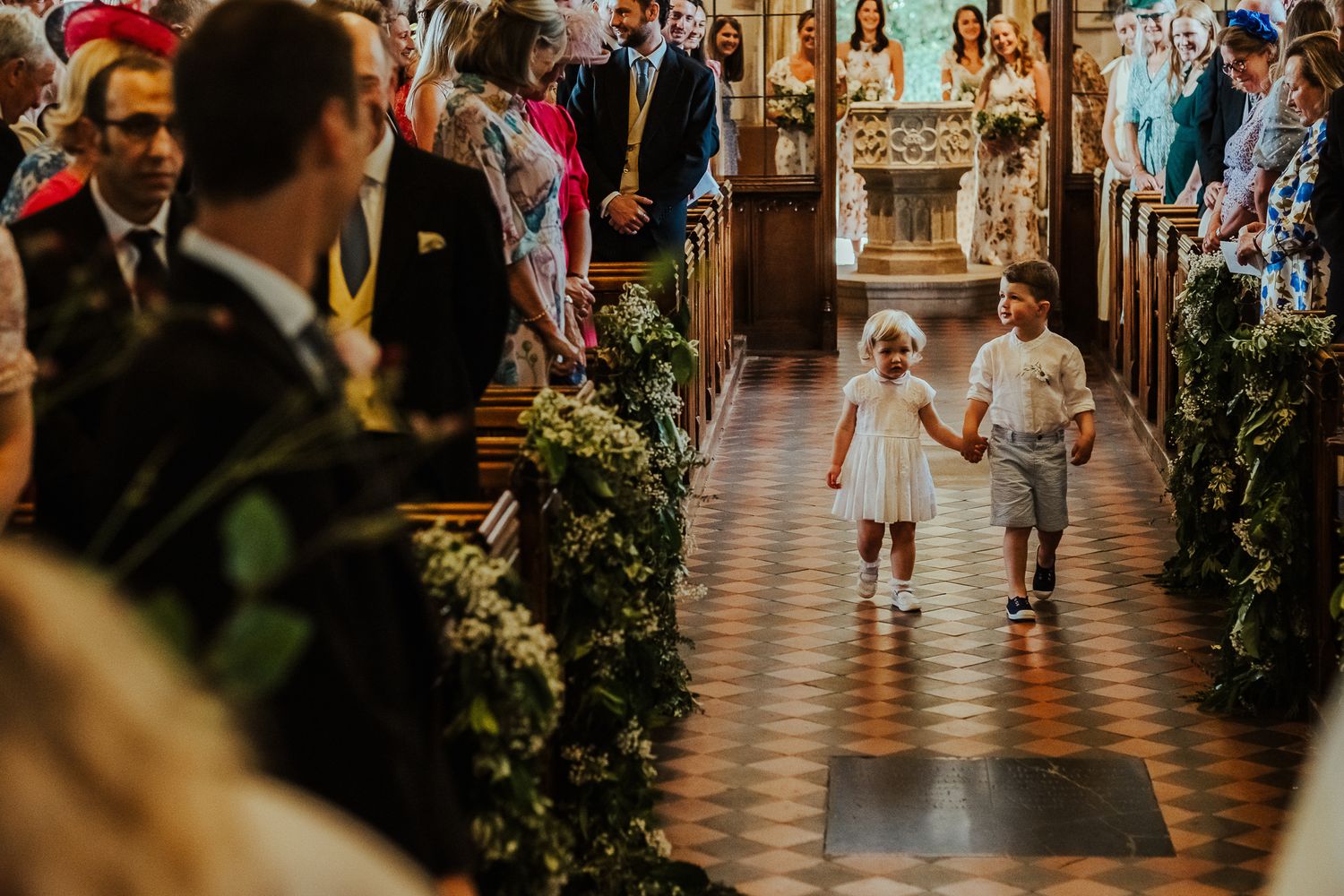 Young children walk down decorated church aisle during wedding ceremony.
