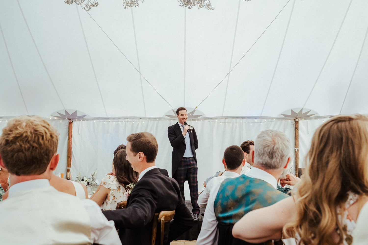 Wedding guests fill a white tent venue during an emotional reception moment.