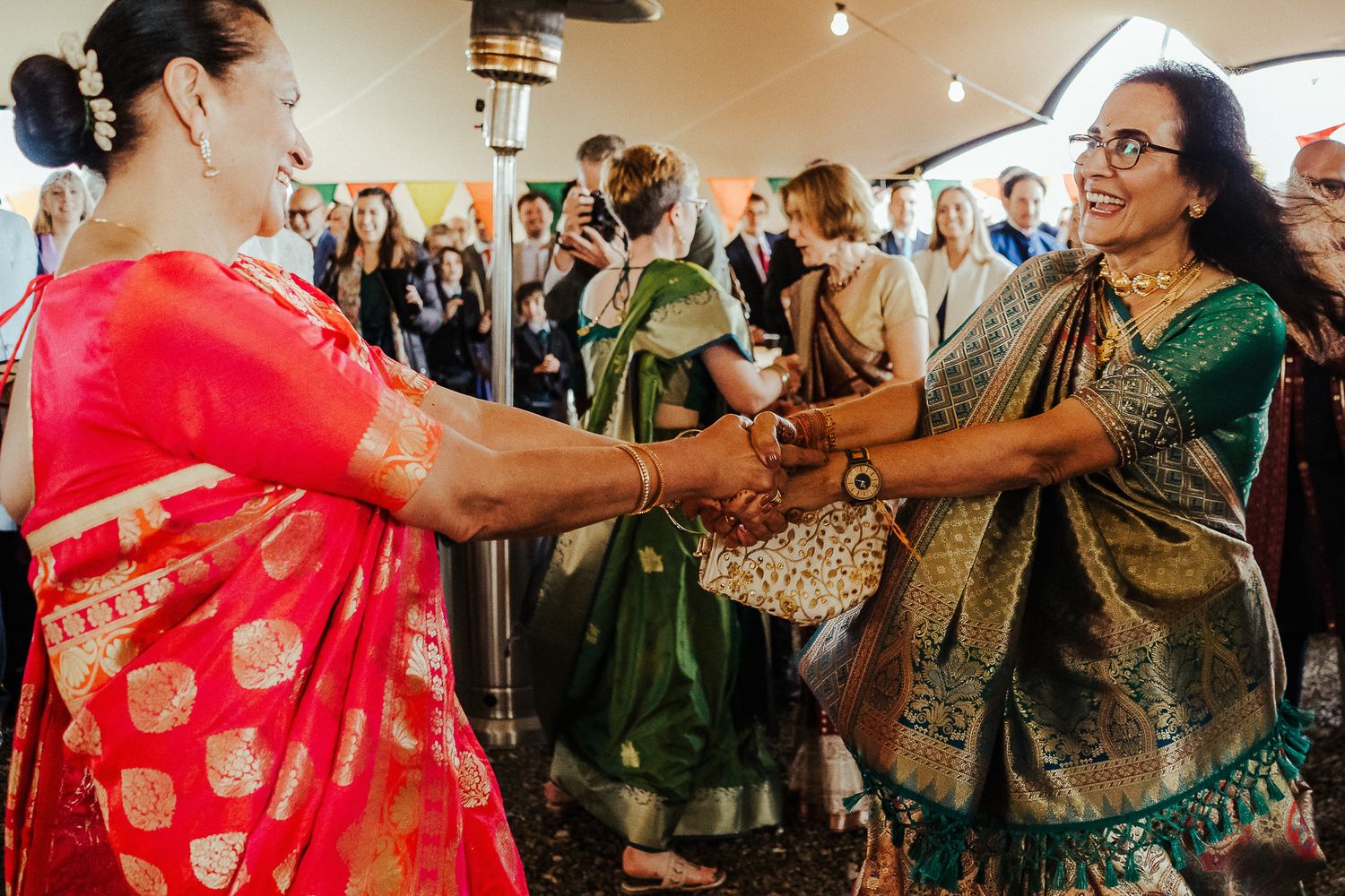 Women in colorful saris join hands in a traditional dance circle during wedding festivities.