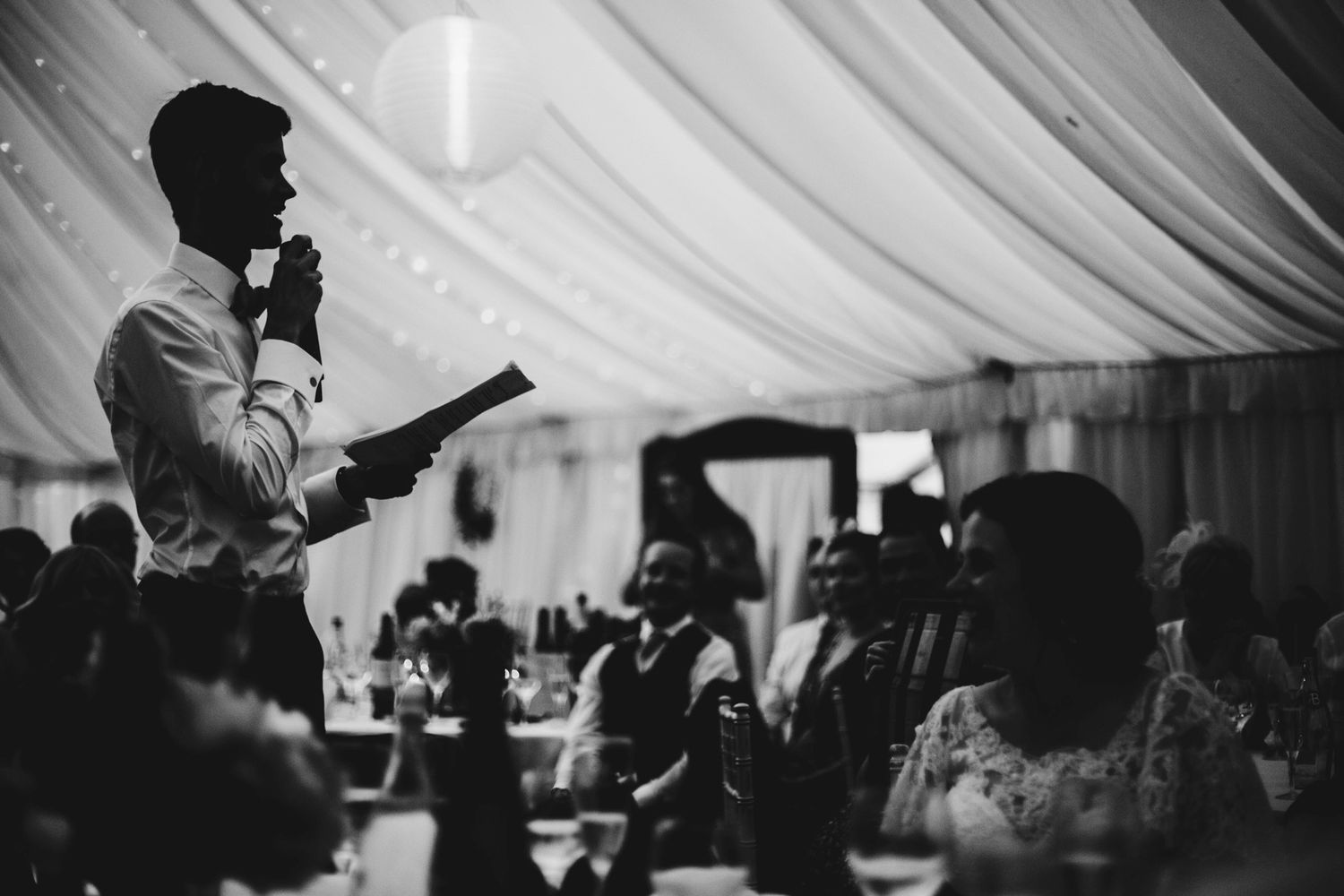 Guest gives a heartfelt speech during a wedding reception in a draped tent venue.