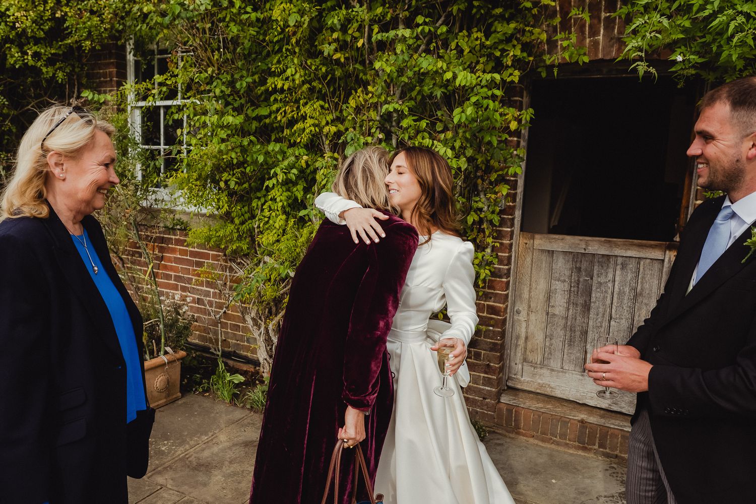 Wedding guests gather in a garden setting to celebrate with the newlyweds during an outdoor reception.