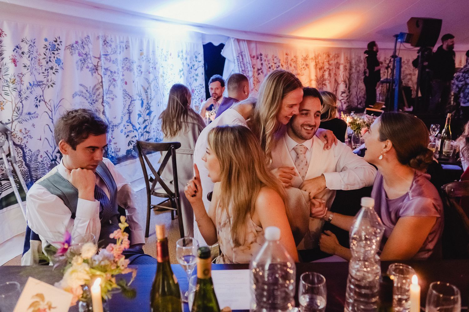 People dancing and celebrating at a lively wedding reception with colorful lighting and decor.