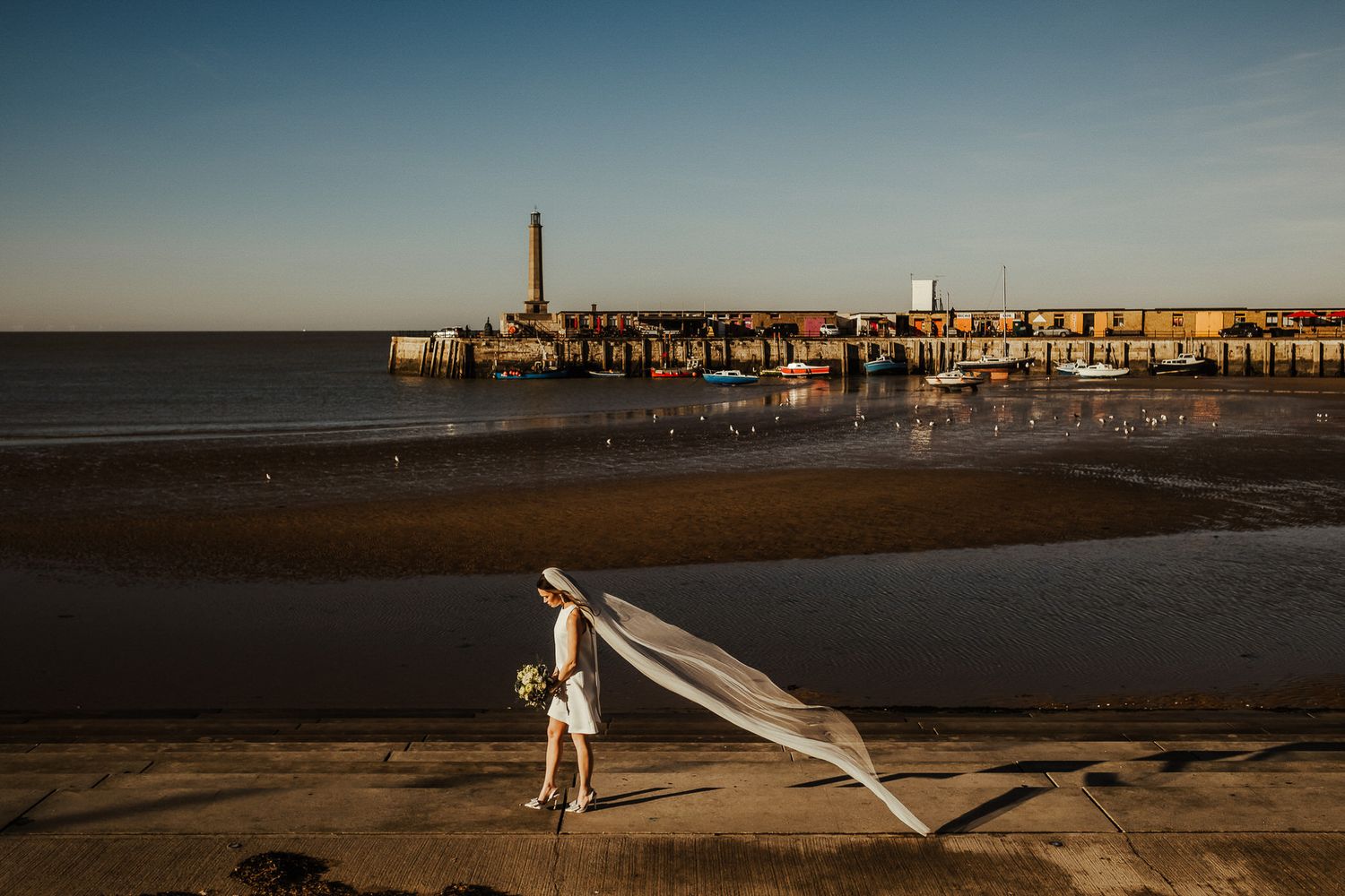 A scenic beach pier at sunset with warm golden light illuminating the coastline and ocean waves.