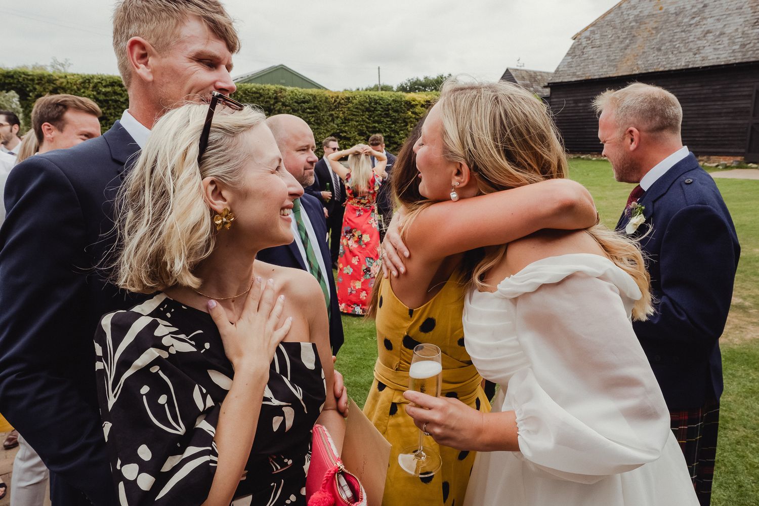 Wedding guests share joyful embraces and greetings during an outdoor reception celebration.