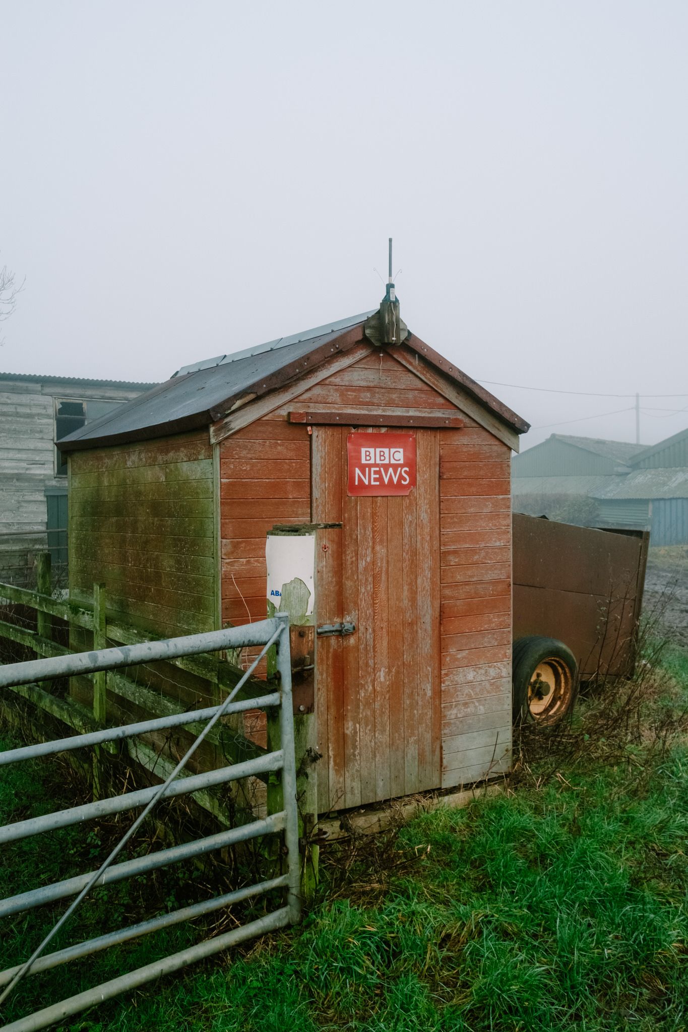 A rustic wooden BBC News shed sits on a hillside with a metal fence in the foreground.