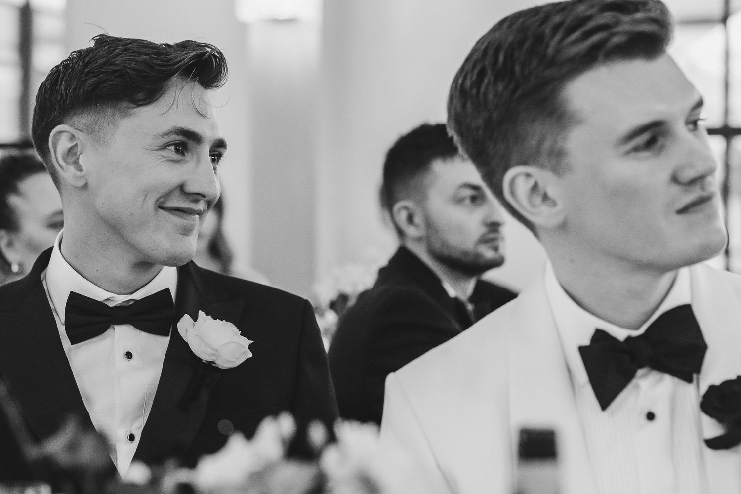 A row of groomsmen in black bow ties and tuxedos stand together in a formal wedding lineup.