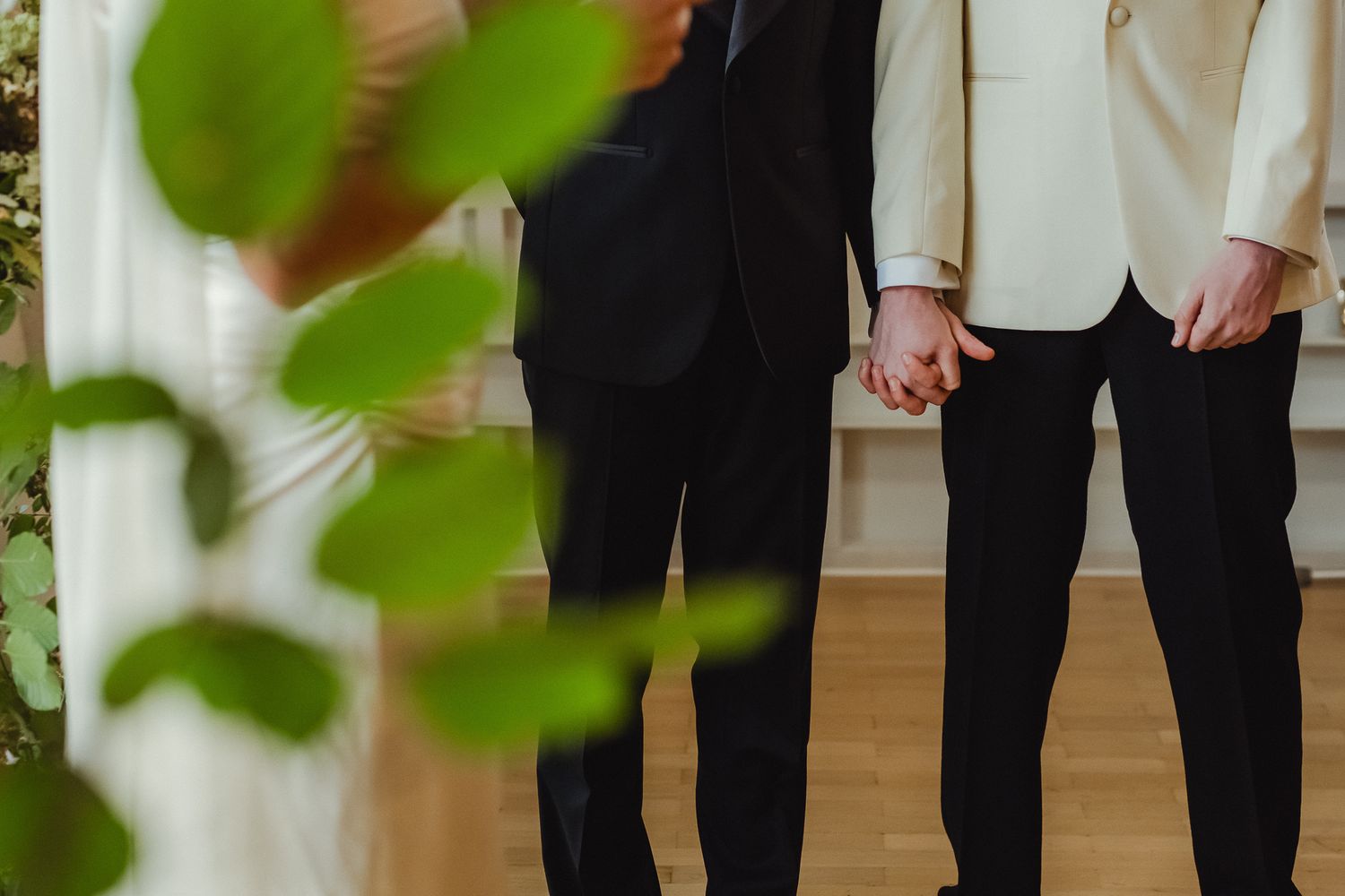 A group of people in formal attire stand together in a line with green leaves visible in the foreground.