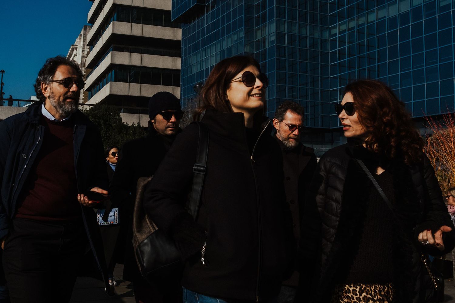 Group of people walking together outside modern glass office buildings on a sunny day.