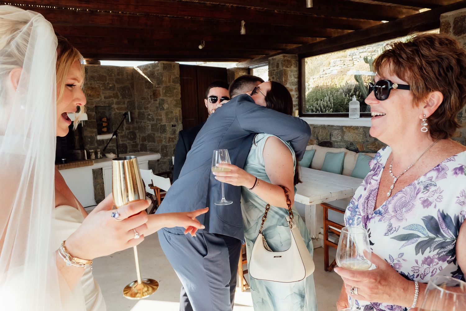 Wedding guests celebrating with champagne, sharing hugs and laughter at an outdoor reception venue.