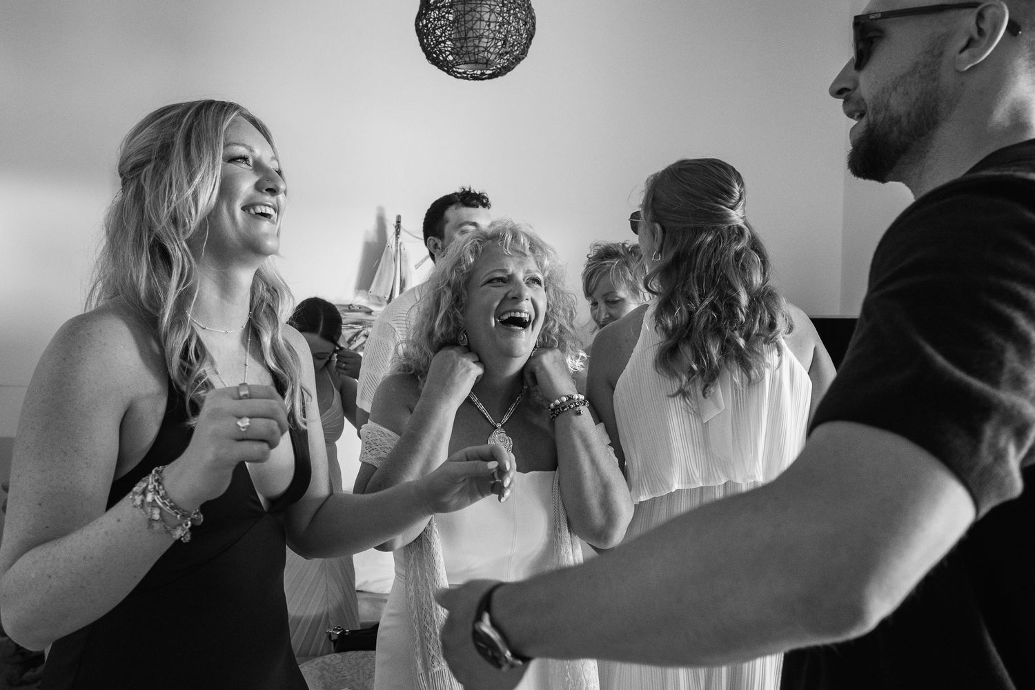 Black and white photo of joyful guests laughing and dancing together at a lively wedding reception celebration.