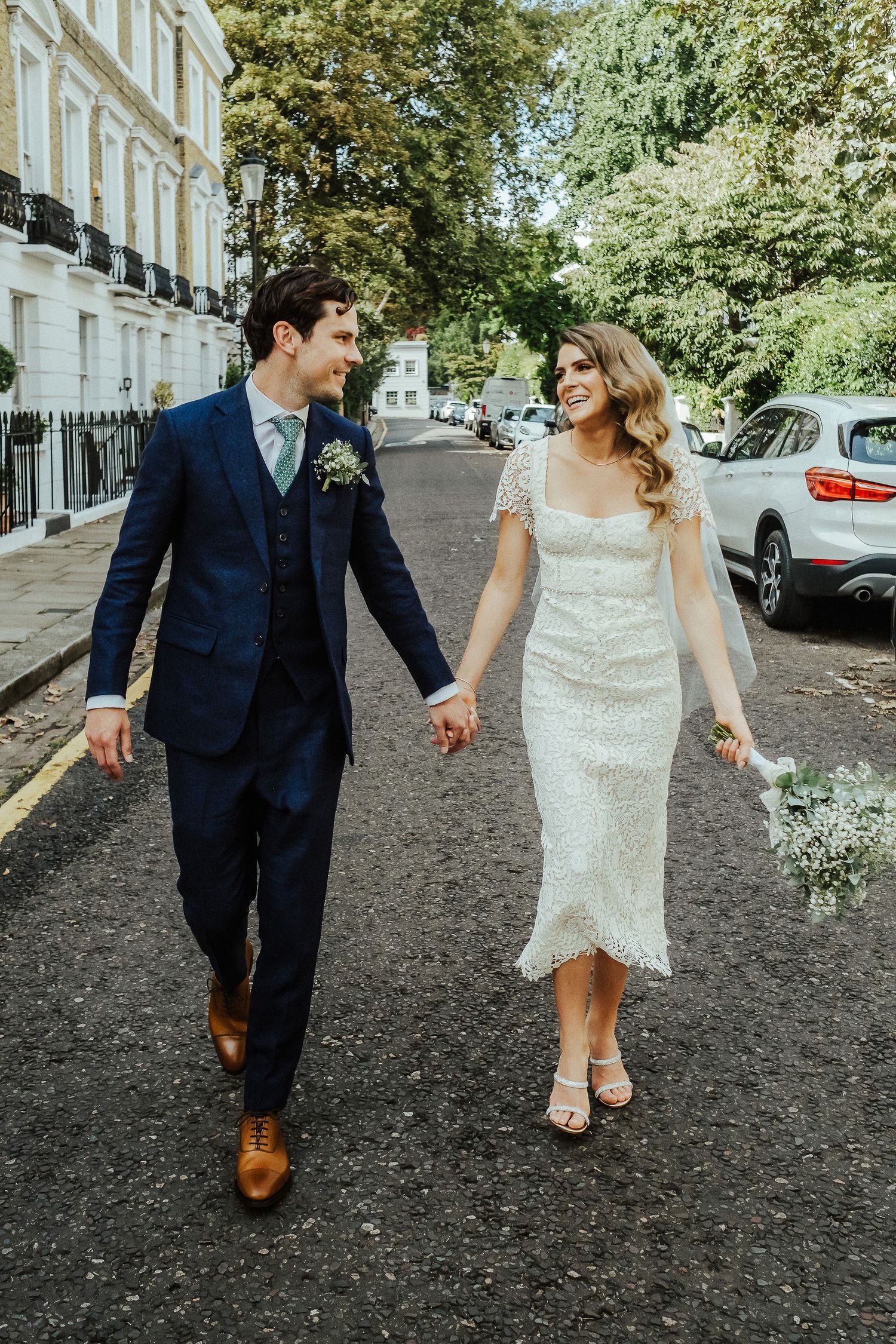 Newlywed couple walking together on a cobblestone street holding hands in front of historic buildings.