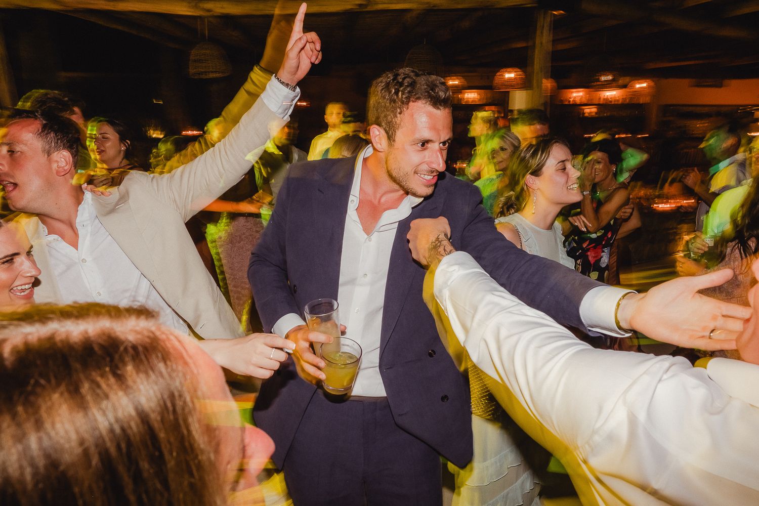 A passionate crowd of partygoers dance together under warm lighting at a nighttime celebration or event.