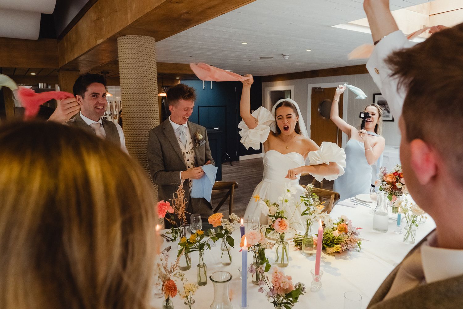 Wedding guests seated at long tables decorated with colorful floral centerpieces enjoy a reception dinner celebration.