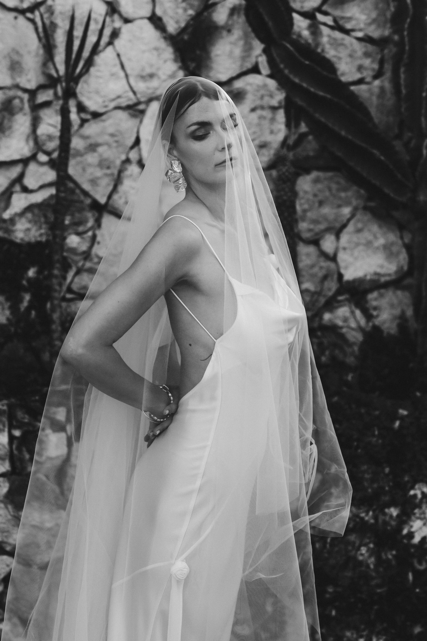 A bride in a white wedding dress and veil poses gracefully in a moody forest setting with dramatic lighting.