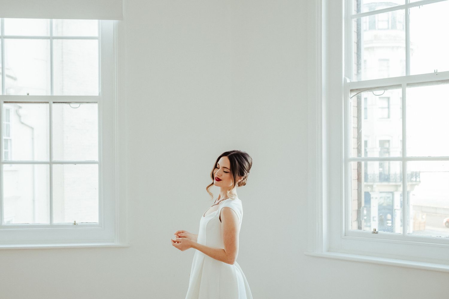 A woman in a white dress twirls gracefully in a bright sunlit room with large windows.