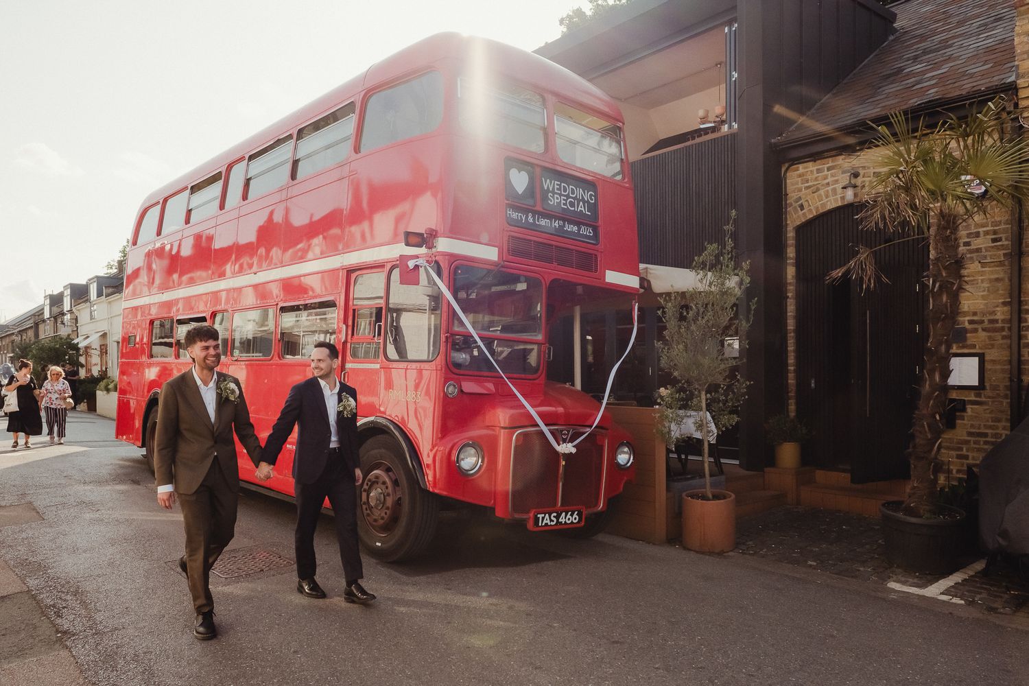 A vintage red double decker bus parked outside a building with people walking nearby.