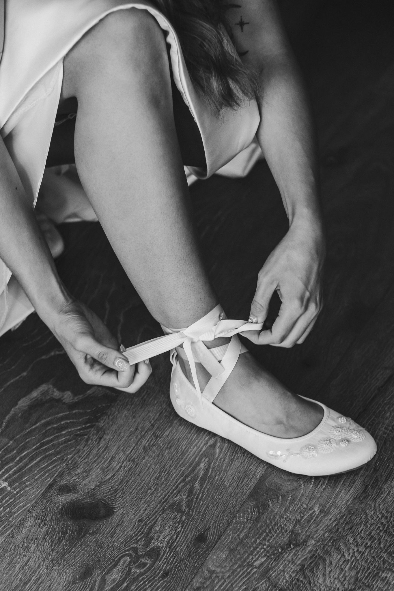 Black and white photo series showing hands putting on white ballet slippers on wooden floor.