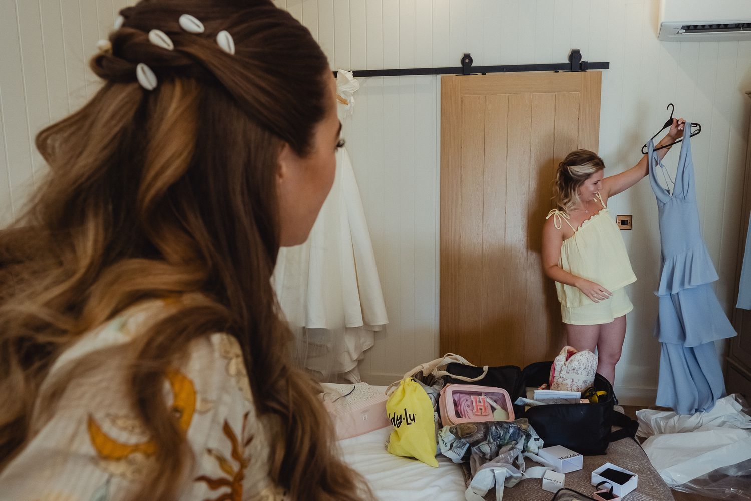 A person in a blue dress hangs a white dress on a clothing rack in a boutique setting.