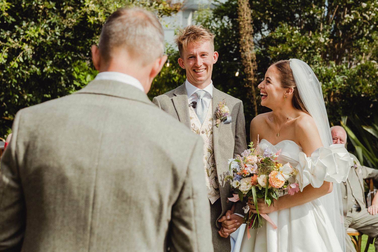 A wedding party celebrates outdoors in a garden setting with champagne toasts and laughter.