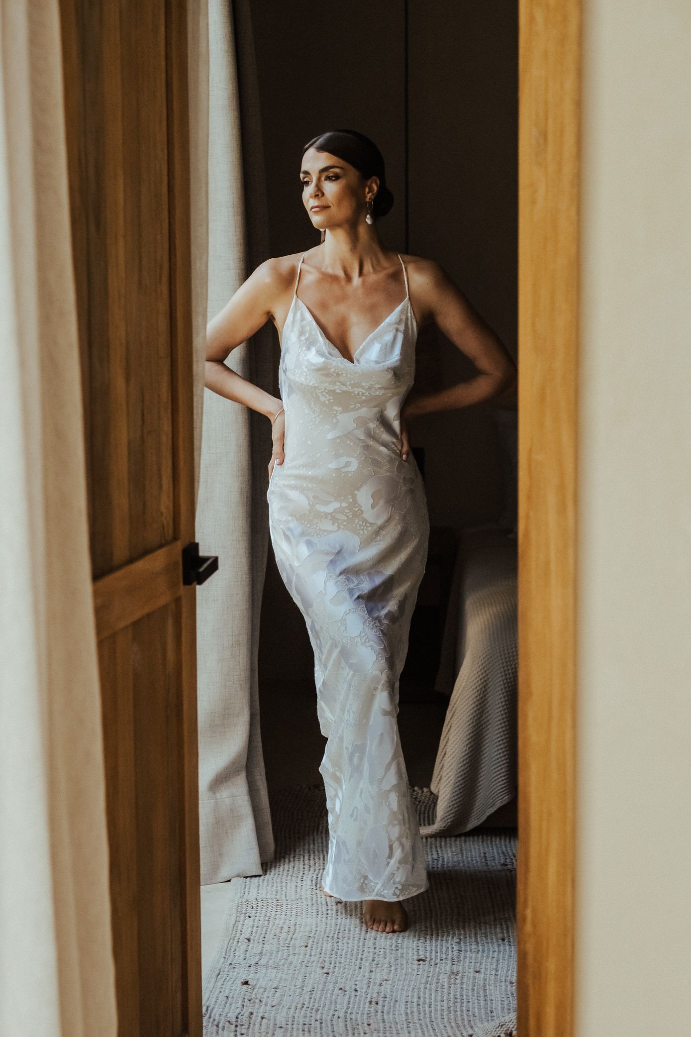 A person in a white wedding dress poses elegantly in front of a mirrored closet door creating multiple reflections.