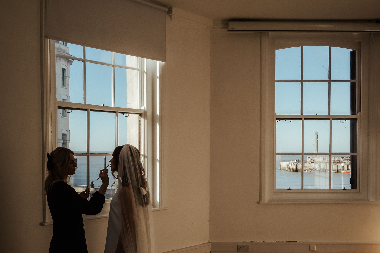 A silhouetted figure stands near a window in a bright white room, creating a dramatic contrast against the light.