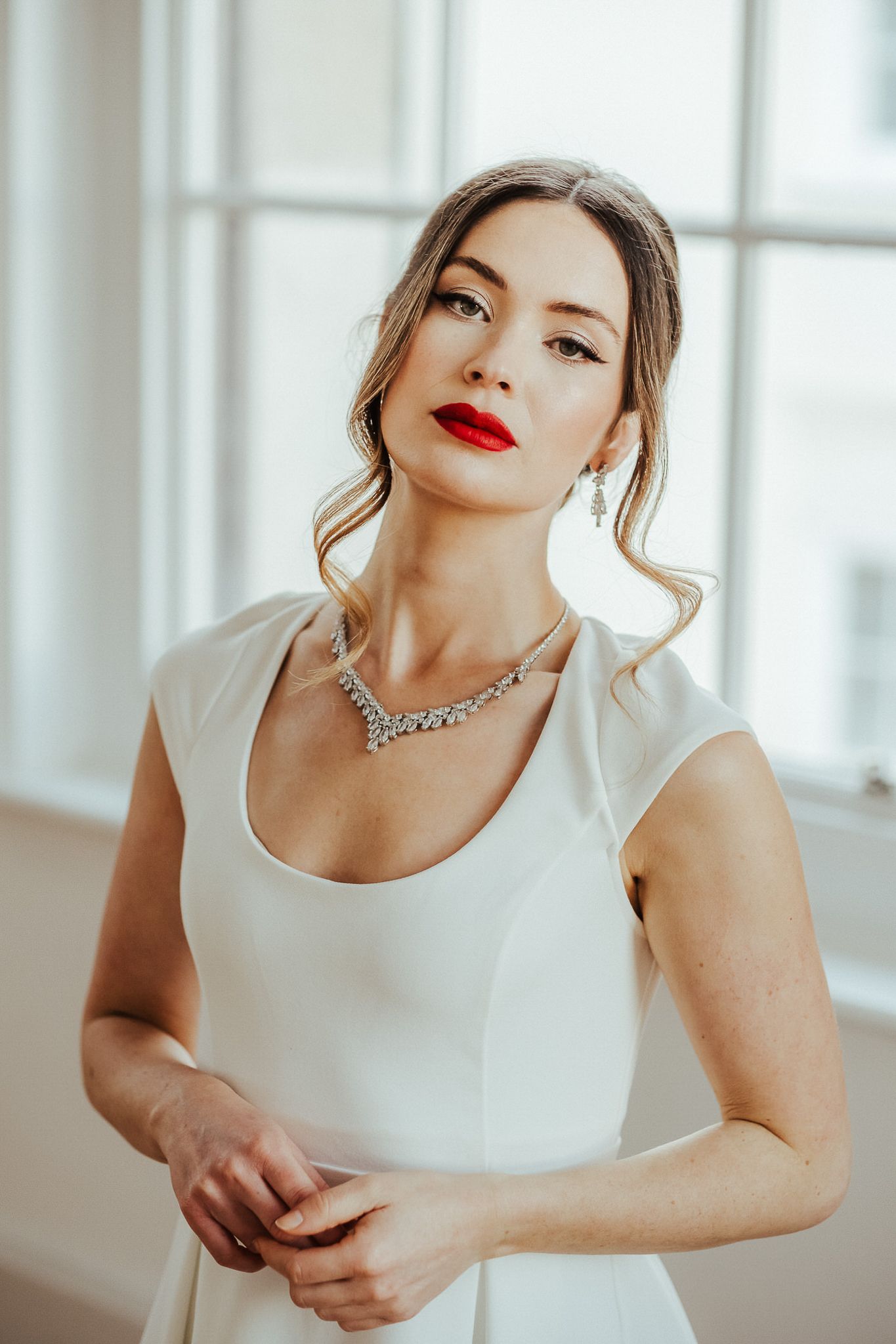 Woman in elegant white dress and red lipstick poses gracefully in bright interior setting.