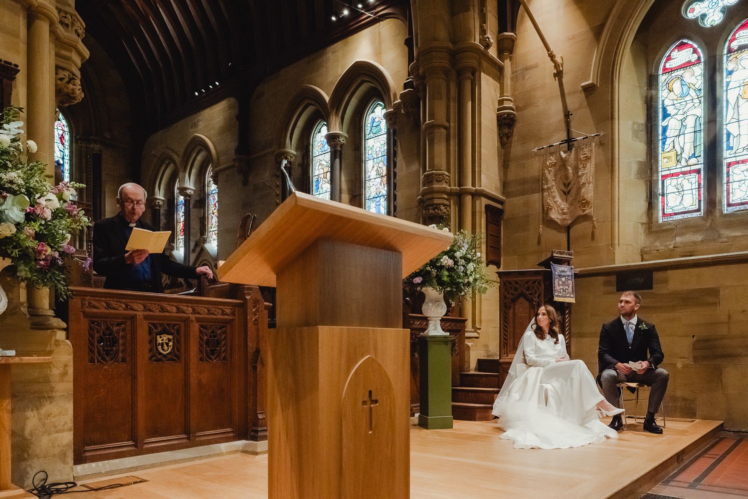 A beautiful church wedding ceremony with stained glass windows and wooden pews in a traditional stone chapel interior.