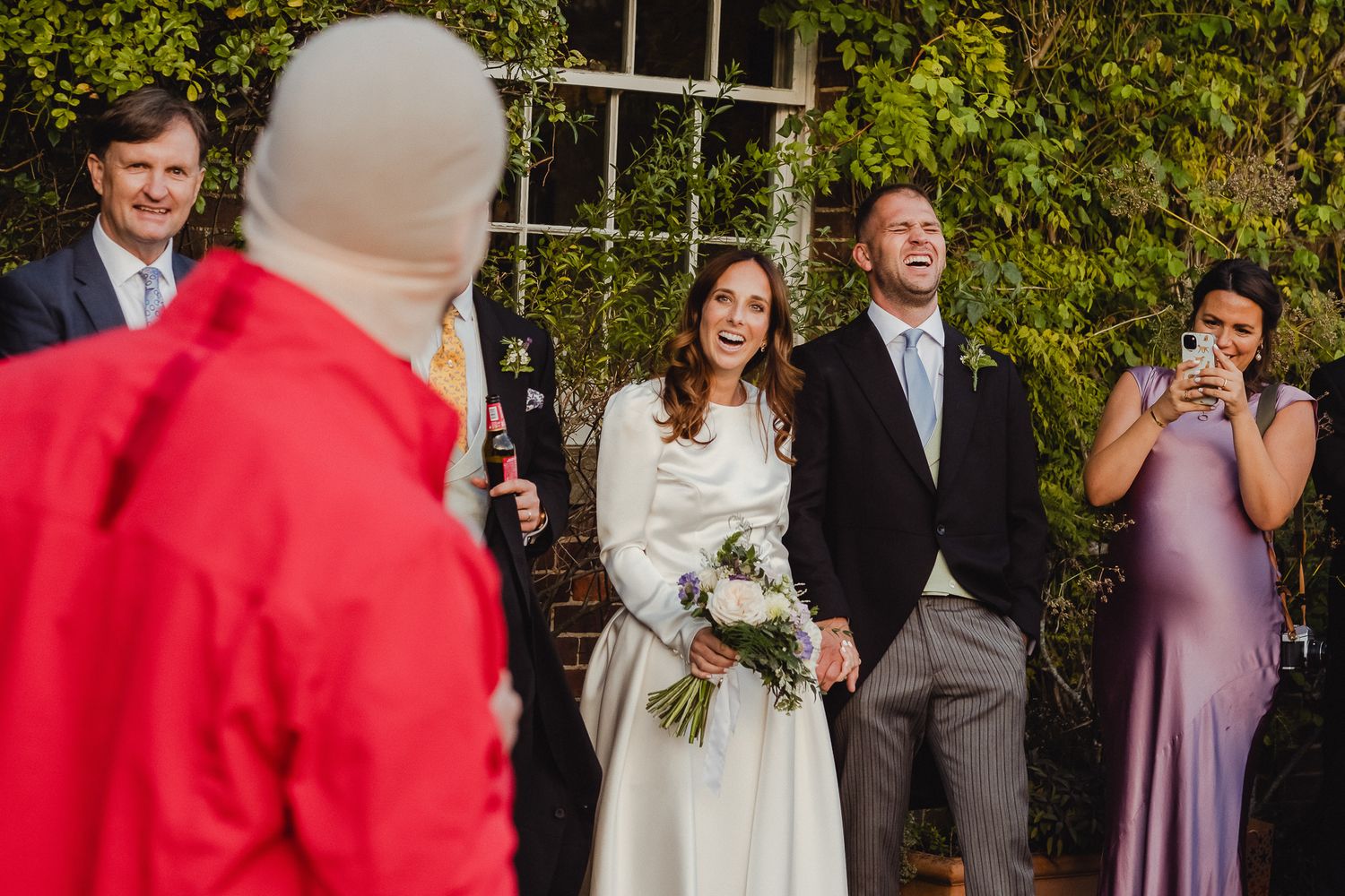 Wedding party in formal attire poses outdoors with bridesmaids in lavender dresses and groomsmen in gray suits.