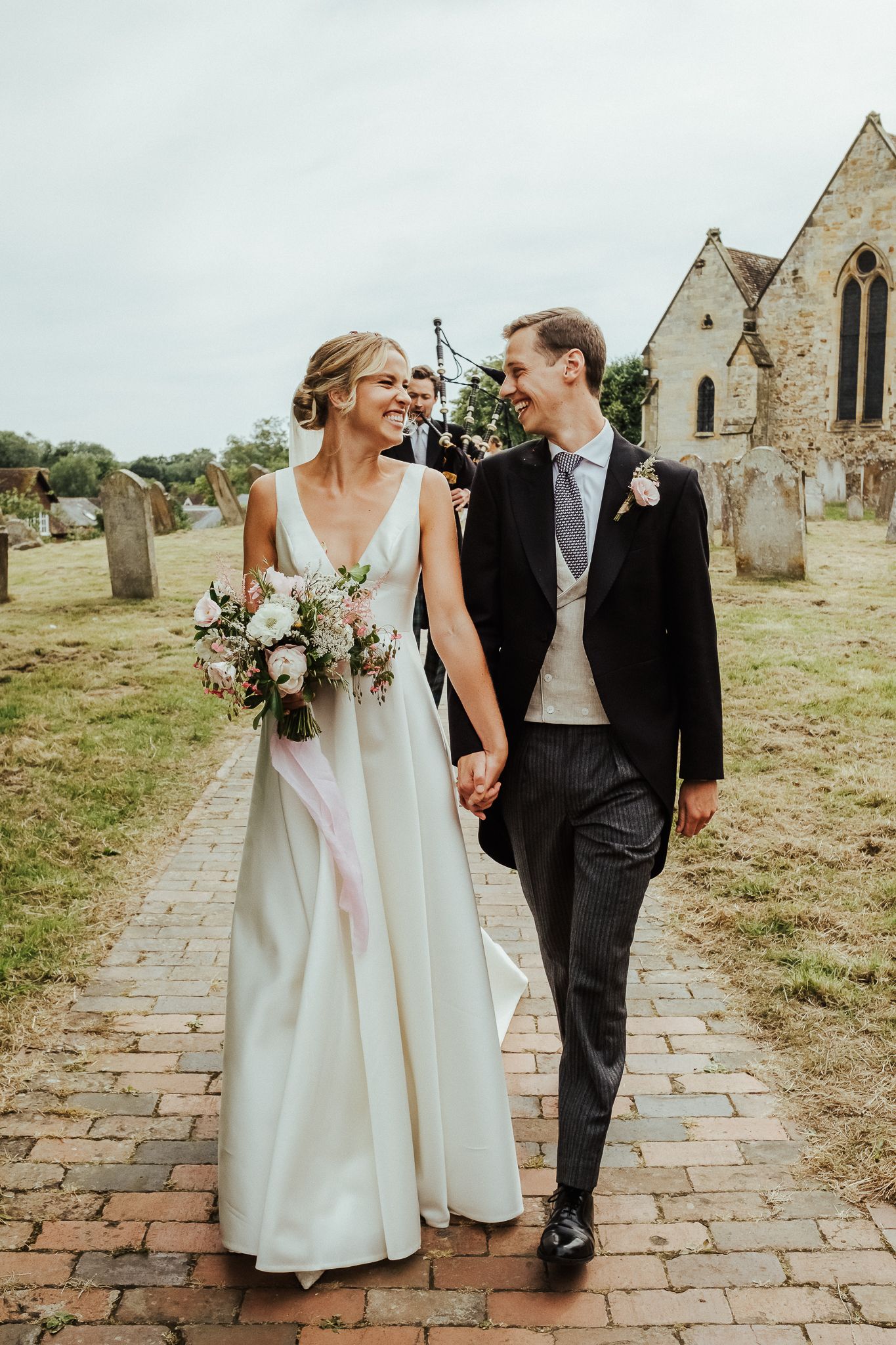 Newlyweds walking hand in hand on a brick path outside a historic stone church.