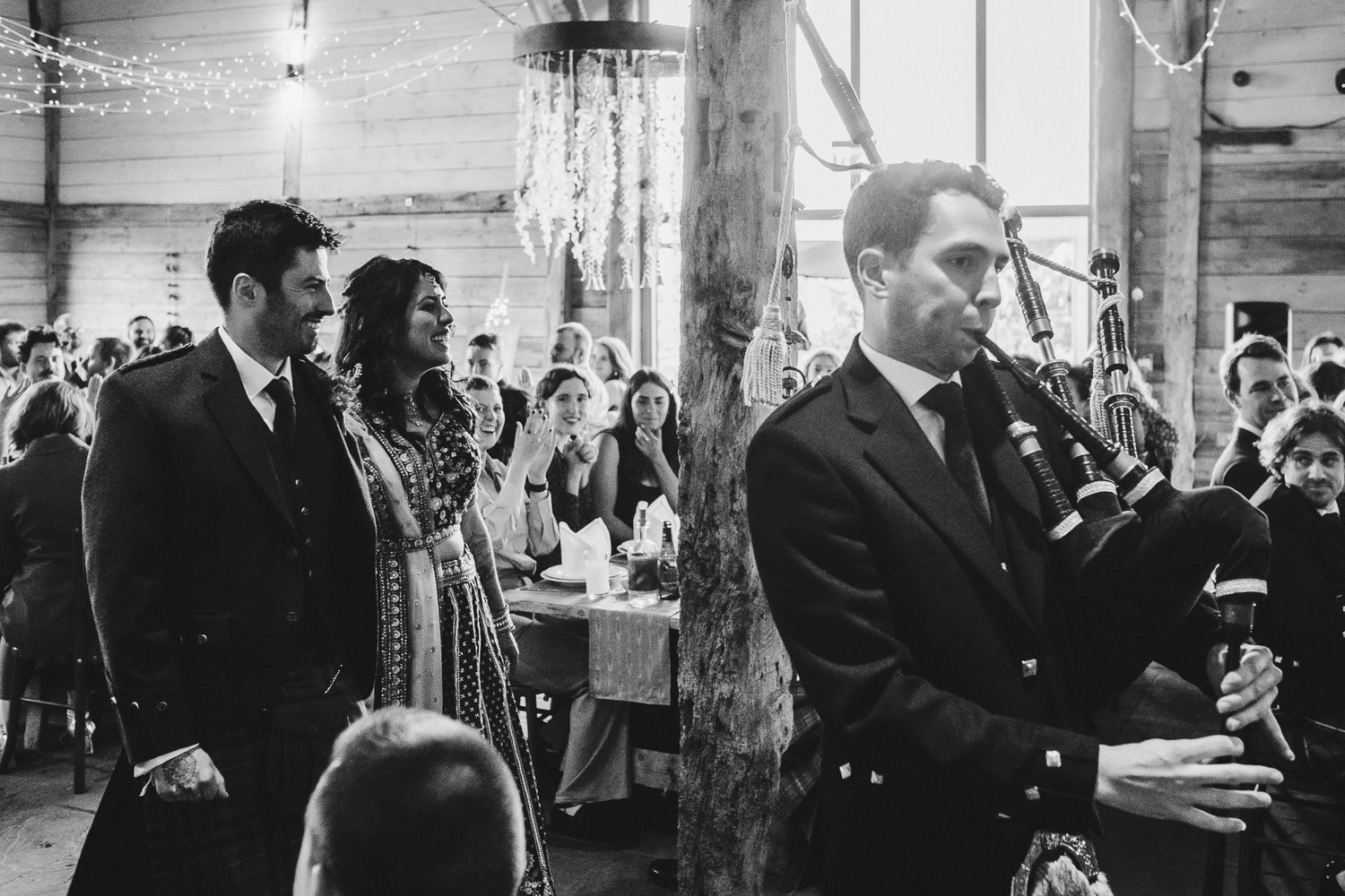A bagpiper performs at an indoor reception while guests watch in the background.