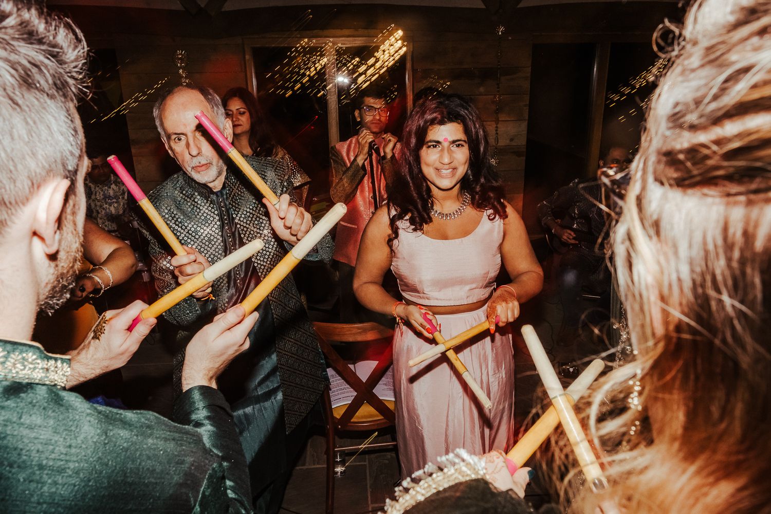 Party guests dancing with drumsticks at a rustic indoor celebration.