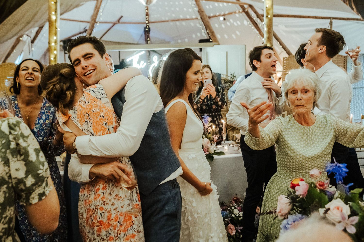 Wedding celebration with guests dancing and celebrating under a decorated tent.