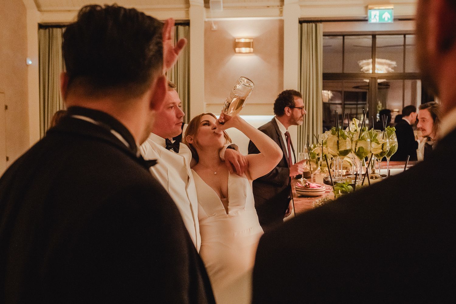 Wedding guests celebrate and raise their glasses during an elegant reception dinner at an indoor venue.