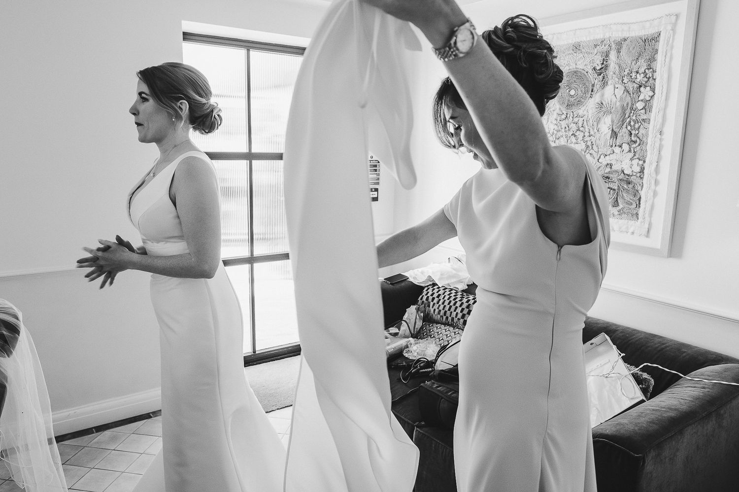 People in formal white attire gather in preparation in a bright indoor room with windows.