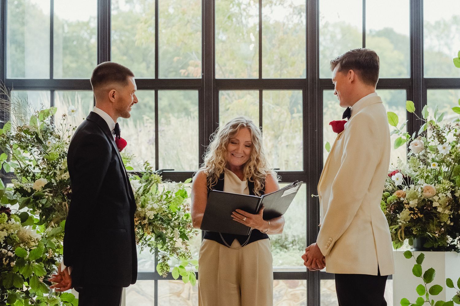 Wedding couple sharing intimate moments during ceremony in sunlit venue with large windows and greenery.