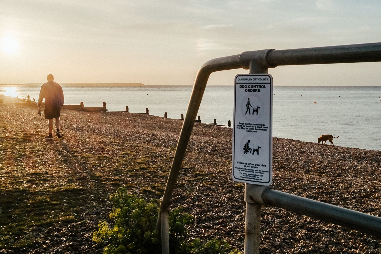 A scenic beach path with warning signs and wooden posts along the shoreline at sunset.