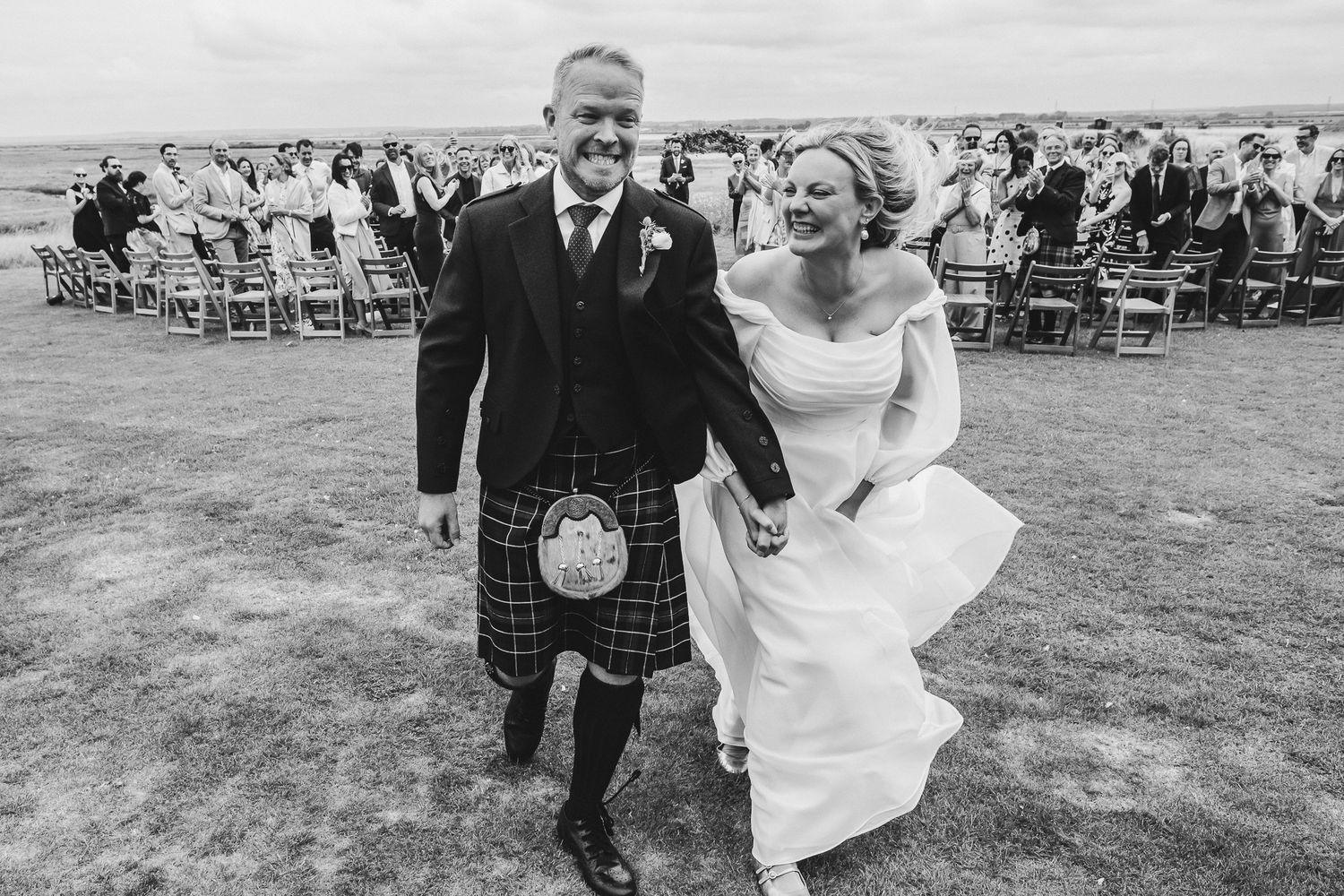 A couple dances joyfully together at an outdoor wedding celebration with guests seated in the background.