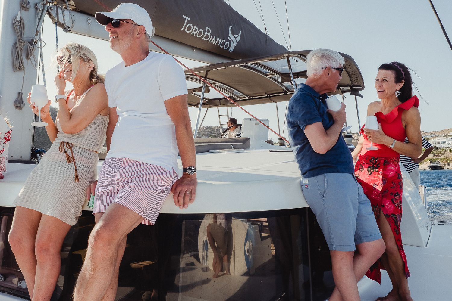 Group enjoying a day on a sailing boat with coastal views in the background.