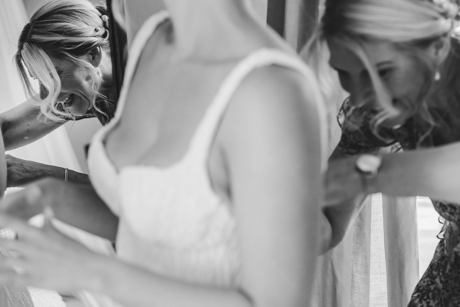 A black and white candid photograph shows wedding preparations with people getting ready in a soft, intimate moment.