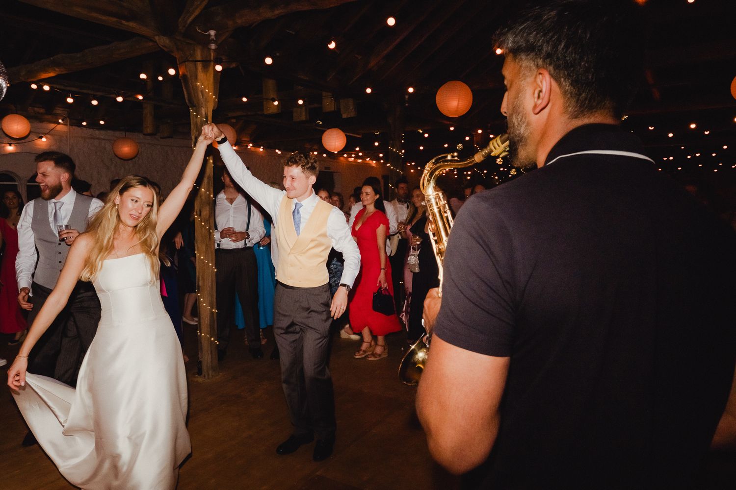 Happy couple celebrates with guests during first dance at their wedding reception under string lights.
