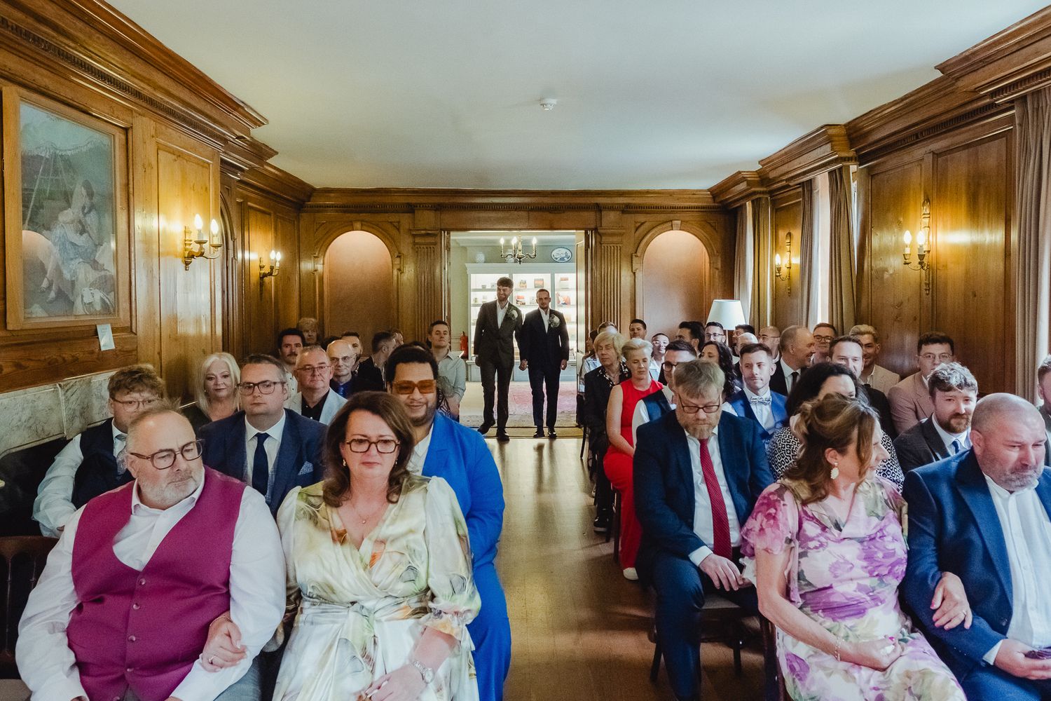 Wedding guests seated in elegant wood-paneled ceremony room with warm lighting and traditional decor.