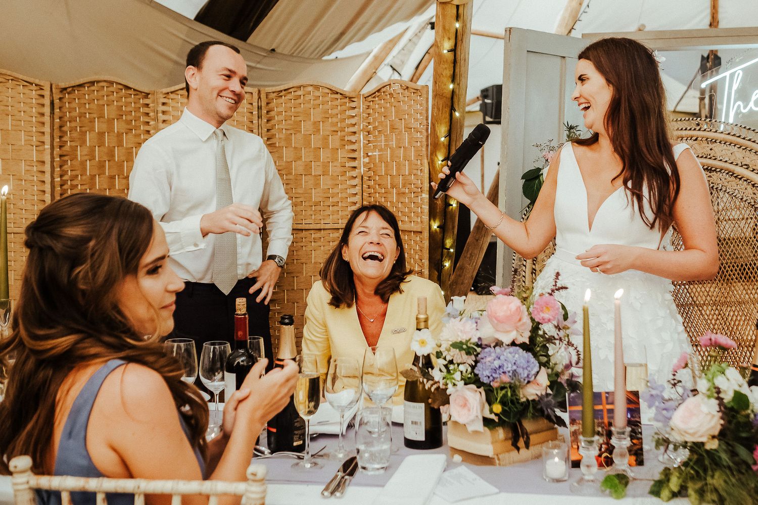 Wedding guests share joyful laughter during dinner reception under tented venue.
