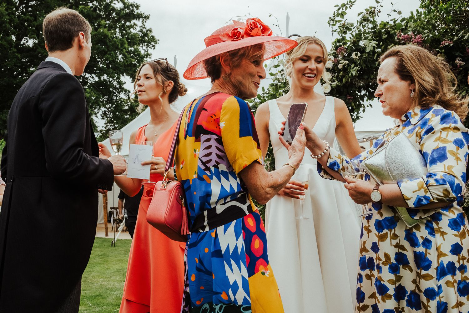 Colorfully dressed wedding guests celebrate outdoors among garden greenery.