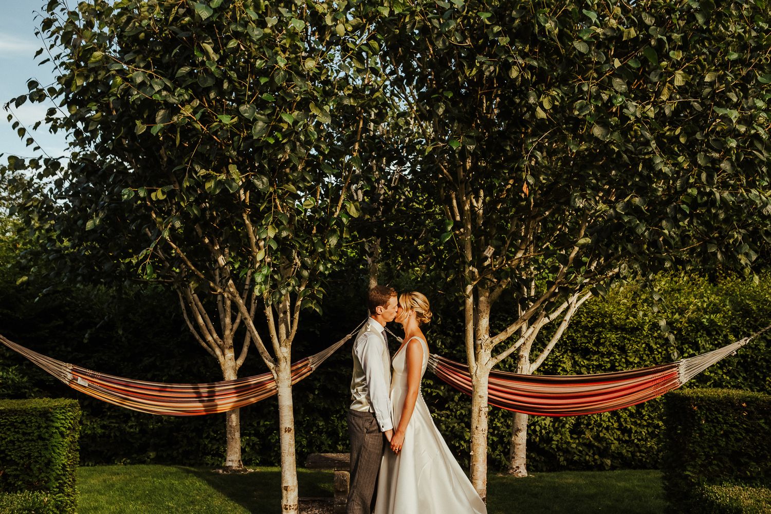 A romantic wedding photoshoot takes place among hammocks in a lush garden setting at sunset.