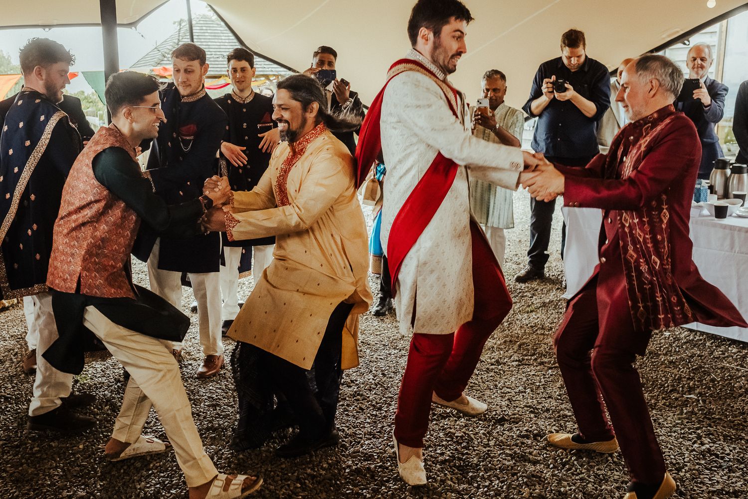Energetic group dance at a fusion wedding celebration with guests in mixed traditional outfits.